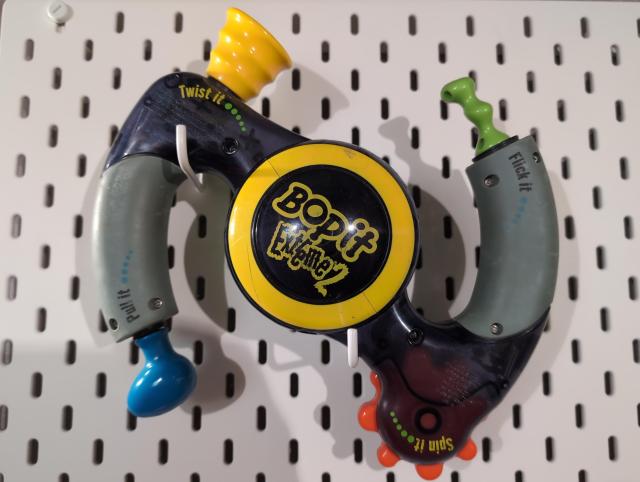 A Bop-It Extreme 2 (very 90s/2000s kids toy) hanging on an IKEA "Skadis" pegboard.