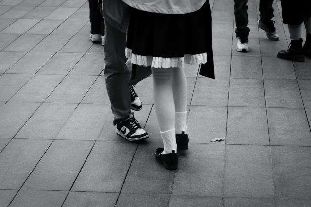 A high contrast black and white photo of dancers on the tiled surface at Bishop's Square in Spitalfields, featuring the feet and legs of a young couple near the camera and of several people further away.