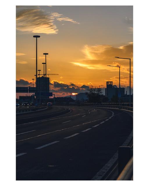 EN: Image shows the almost empty roadway of the Floridsdorf Bridge in Vienna, Austria. In the background, the setting sun is partially obscured by some clouds, illuminating the scene.

DE: Bild zeigt beinahe leere Fahrbahn der Floridsdorfer Brücke in Wien, Österreich. Im Hintergrund ist die von einigen Wolken teilweise verdeckte, untergehende Sonne abgebildet, die die Szene beleuchtet.