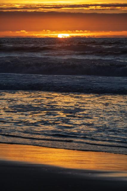 The sun sets behind the sea, its reflection golden on the beach sand. [Fuji X-T5 / Tamron 18-300]