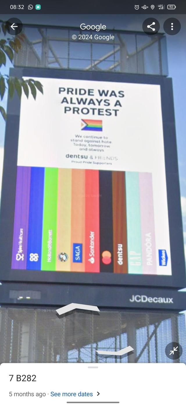 a sign reading "pride was always a protest", followed by a progress flag where each coloured stripe has been labelled with a company's logo. the black stripe is mastercard.