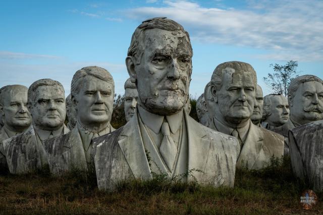 A large bust of Woodrow Wilson is in the foreground, its face peeling away and stained by time. Behind it rows of other presidential busts are visible.