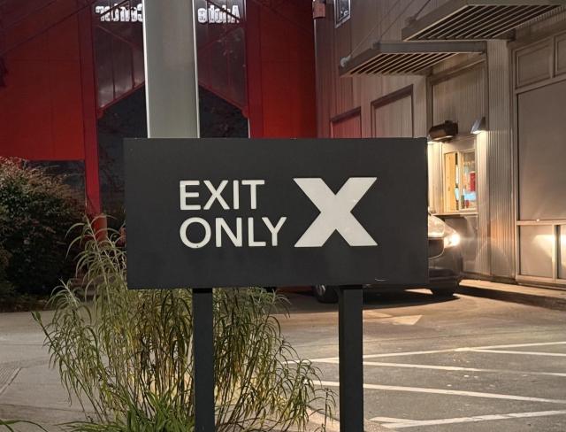 A sign with the words "EXIT ONLY X" is placed in a parking lot near a building.