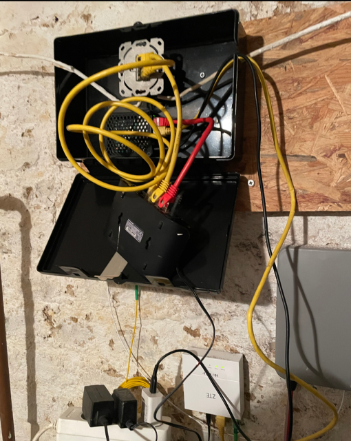 box mounted on a wall with a rounter, a switch and a lot of ethernet cables inside
