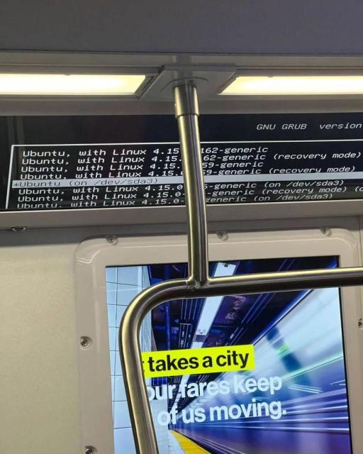 There is a wide screen on a metro train which shows GNU GRUB with a list of Ubuntu boot options.