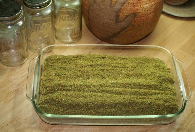 A baking dish full of chili powder, three quart jars, and a handprints lamp base on a table top.