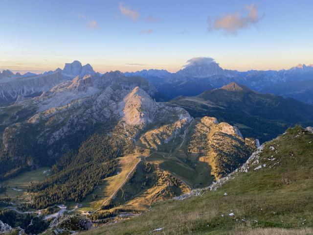 A weathered mountainous landscape lit by the orange rays of the rising sun. The trees covering mountain slopes cast long shadows across the terrain. 