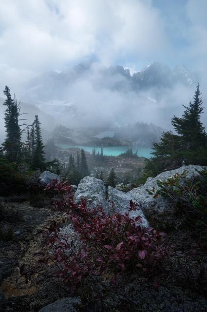 Looking out from a ride towards a glacial lake and jagged mountains. The light is dappled on the lake and fog partially obscures the peaks.