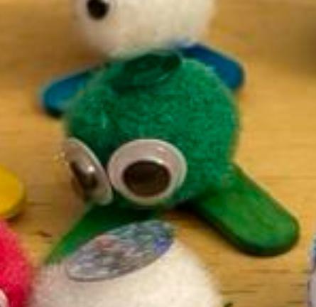 An inset from the original photo highlights one green fuzzball with google eyes and green feet. The eyes are wide and slightly downcast, as though in deep thought. 