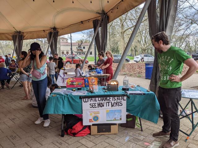 Table setup outdoors under a big canopy with demo items and a sign taped to the table that says Climate change is real See how it works