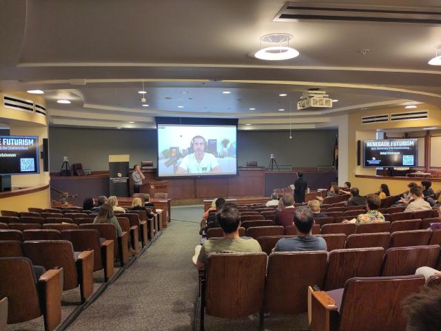 Balaji Srinivasan on a screen in a sparsely populated auditorium.