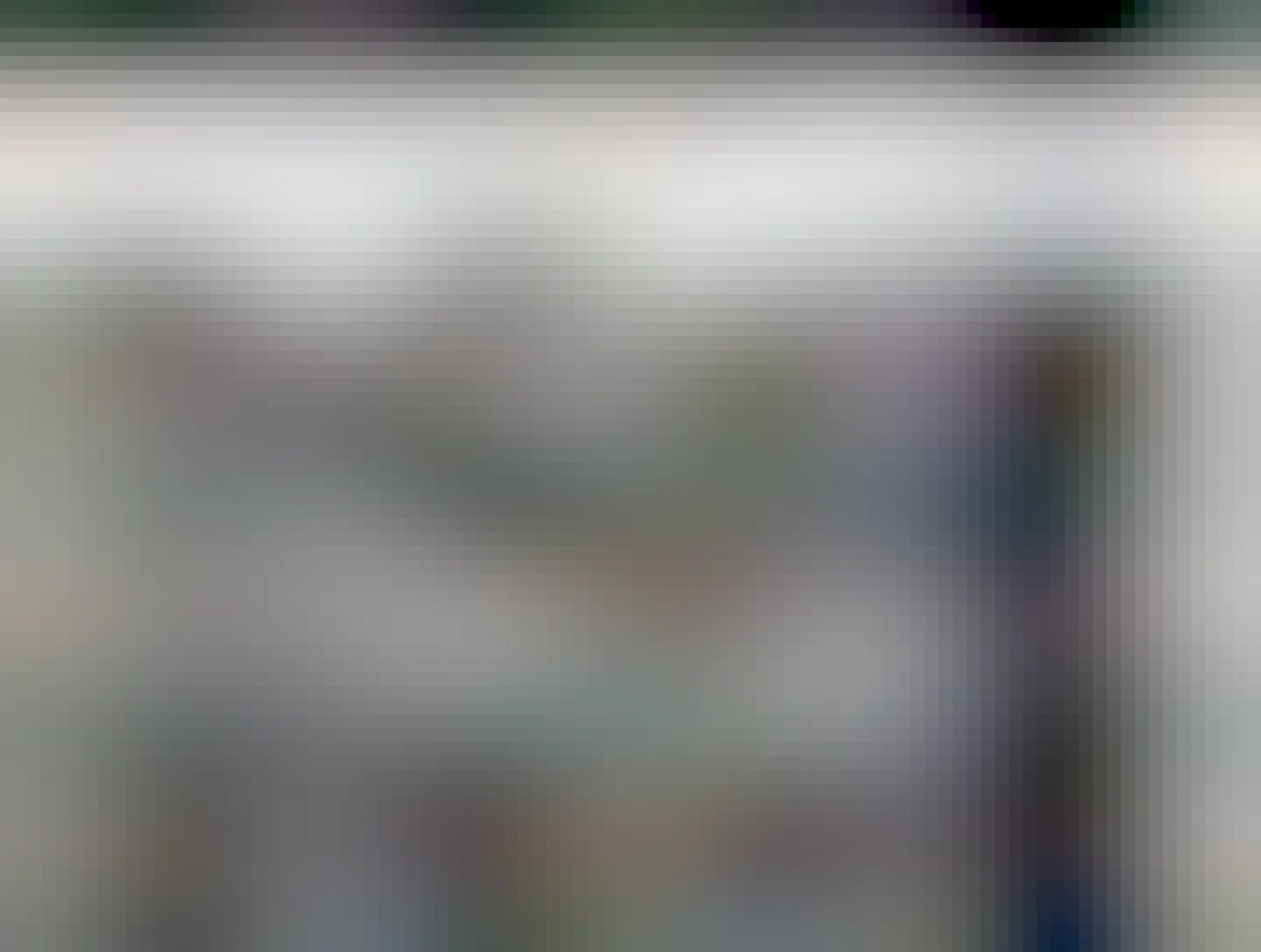 A black and white picture showing a black labrador sitting in a yard beside a dog house and near a dog bowl.  The picture looks sad, and the dog looks sad.