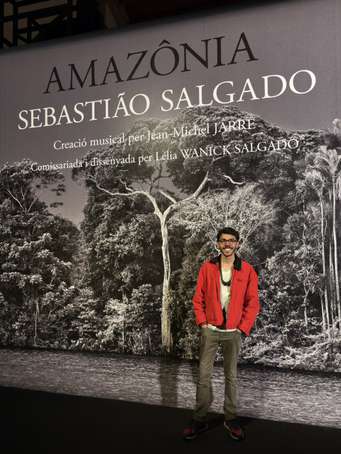 Me you wearing a red jacket, gray T-shirt and a coconut collar in front of the Sebastiao Salgado’s exhibition Banner in Barcelona, Spain