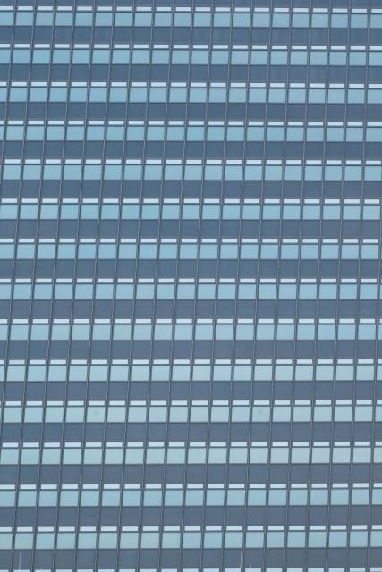 A photo up a wall of windows. Each window has a white strip above it as well as a bigger blue grey patch. The windows itself are pale blue, it’s a huge wall with plenty windows 