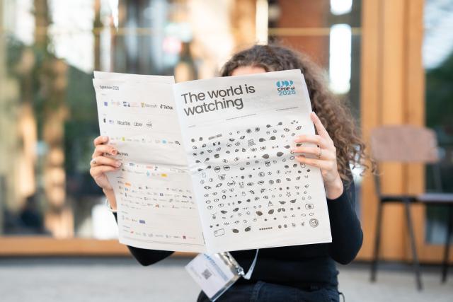 A person reads a newspaper headlined "the world is watching" - the same artwork features on the cover.