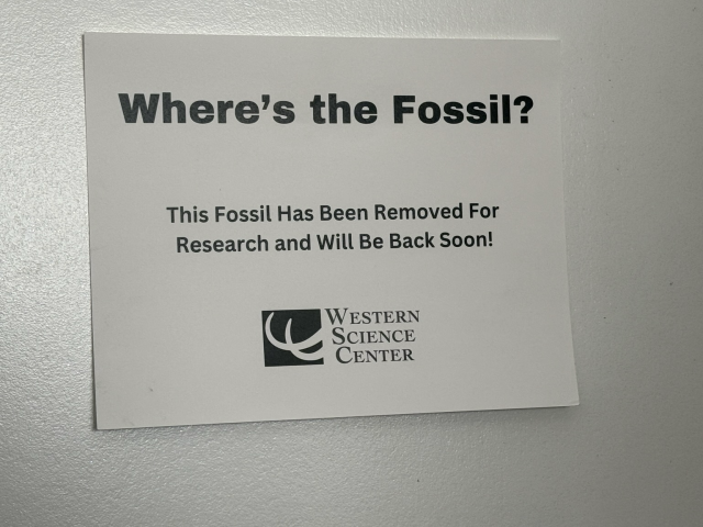 Sign attached to a door that reads “Where’s the Fossil?? This fossil has been removed for research and will be back soon!” Followed by the Western Science Center logo. 
