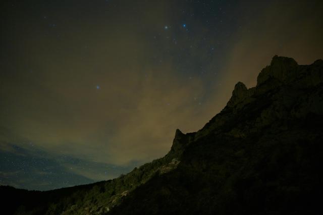 A mountain landscape at night, with some clouds and some stars visible.