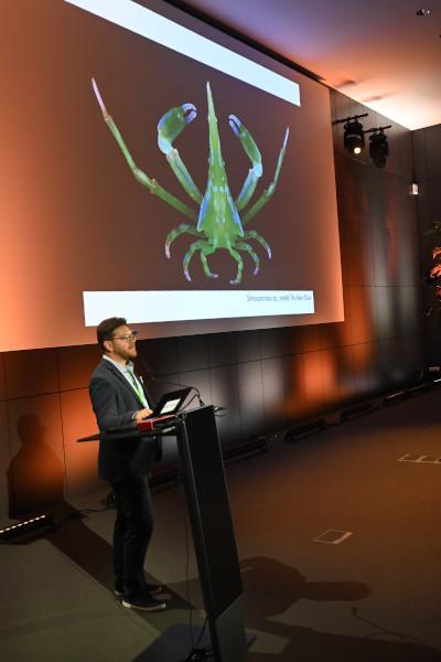 The opening ceremony of the TCS summer meeting, with Dr. De Mazancourt explaining the origin of the logo. A crab, green in color, Simocarcinus simplex, is displayed on the screen in the background.