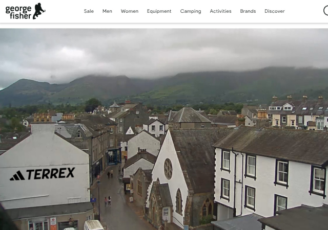 Looking down a damp street with mainly white buildings both sides. There are fells in the background capped in cloud.