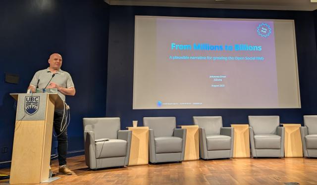 Johannes stands on stage in front of the screen which reads From millions to billions - a plausible narrative for growing the open social web
