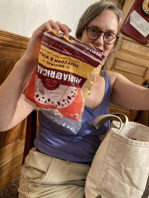 A white woman in a purple tank top and glasses holds up a tortilla bag and her iPhone XR