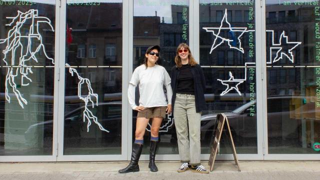 Marie & Dasha are posing in front of the glass doors of iMAL. They're both wearing sunglasses because it's that sunny. The windows are decorated for our current exhibition with drawings, the title "I am vertical but i would rather be horizontal" and excerpts from the eponymous poem.