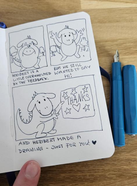 A small open sketchbook with fountain pen next to it. (It's a Kaweco Sport in turquoise)
The comic on the page shows:
Image 1: a little dragon that is hiding his face with his arms. Text: Heribert is a little overwhelmed by the feedback.
Image 2: the little dragon waves his arms and smiles. Text: But he still wanted to say hi!
Image 3: The liddle dragon smiles and holds up a drawing, childlike with a heart and stars that says thanks in big letters. Text: Heribert made a drawing - just for you! and another heart drawn.

The comic is just line and ink, no color, but looks adorable and very simple.