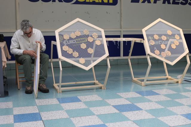 A person in a white shirt threading wire through a hexagon-based sculpture in a shopping centre corridor