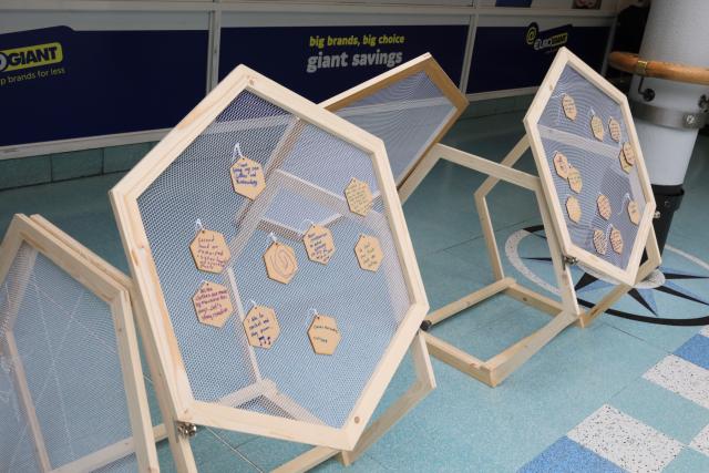Hexagonal sculptural object with small hexagons hanging from it, and each has some words or a drawing