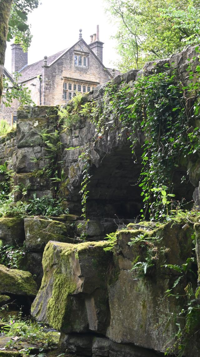Bridge over a steam with an old hall in the background. Lots of ivy and ferns growing in the bridge 