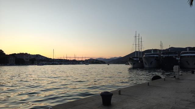 view North fro Groz near Dubrovnik. quay in the foreground with a bollard three medium cruise ships and s small square rigger moored up on the right. calm water straight ahead with sun going down behind the hills on the far shore
