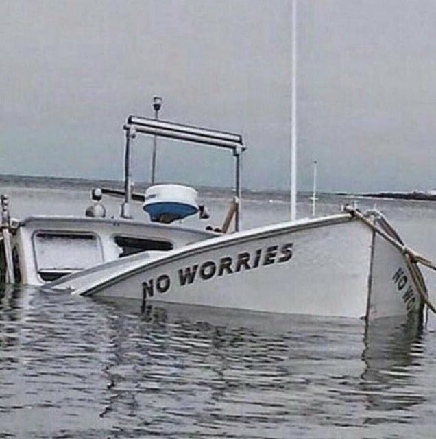A photograph of a boat sinking, 70% under the water. On its front is the name "NO WORRIES" just above the waterline