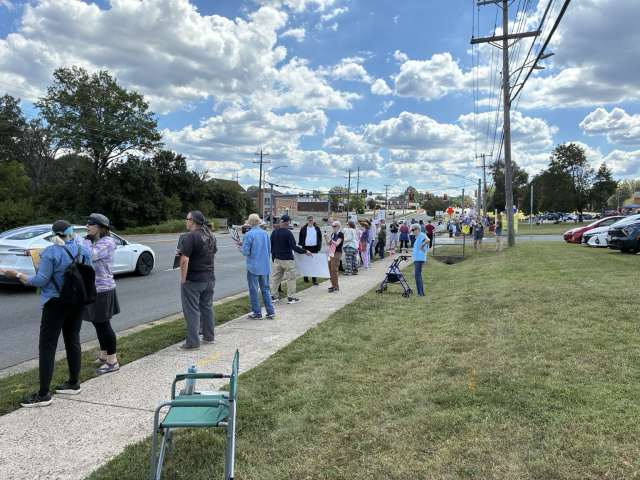 Beautiful blue sky with fluffy clouds and 2 of 3 blocks lined with protesters with American flags and handmade signs.