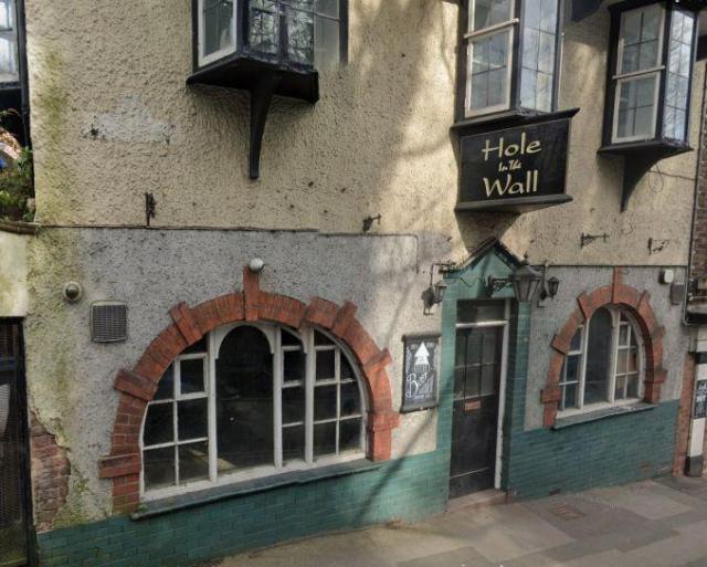 Street view image of a small pub on a hill named 'hole in the wall'