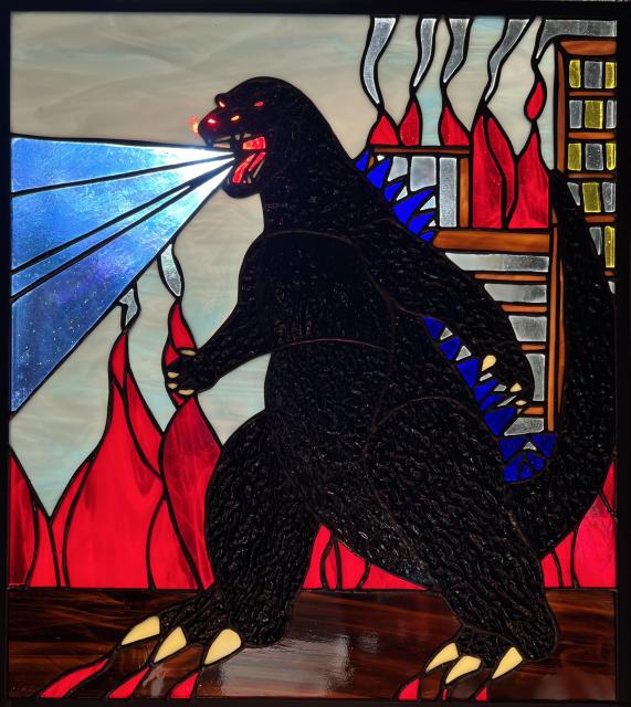 Stained glass of Godzilla with buildings and fire in the background. Godzilla has atomic breath and textured glass for its body.