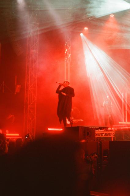 Daniel Tompkins, the lead vocalist, singing into a raised microphone, illuminated by red light.