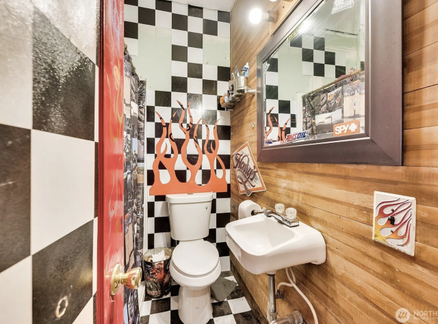A bathroom with the walls painted checkerboard black and white, with fake flames coming out of the top of the toilet.