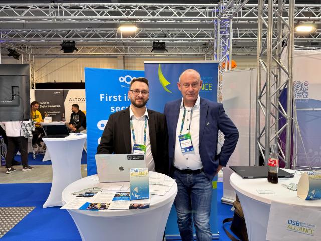 Marius Quabeck (links) und Markus Wachovius (rechts) stehen an einem Messestand der Open Source Business Alliance auf der FutureTec 2025. Auf den Stehtischen liegen Flyer, Materialien und ein Laptop. Hinter ihnen sind Banner von Nextcloud und der OSB Alliance zu sehen. Im Hintergrund befinden sich weitere Messestände und Besucher.