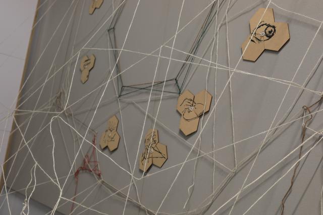 Detail showing lots of interwoven string with drawings on timber of an eye and hands visible on the wall
