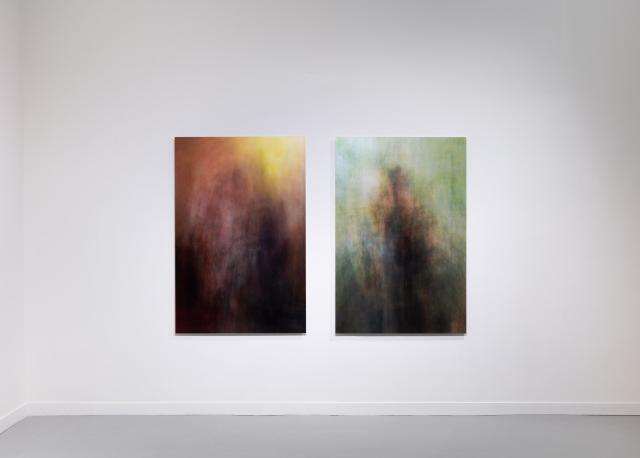 Two of the prints in the exhibition hang next to each other on a white wall. On the left the image is a golden and warm abstract. On the right a the image is cool, green/blue, and dark.