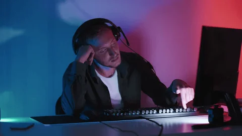 a stock photo of a weary-looking fellow wearing headphones at a computer. he is dejectedly pressing a key on his keyboard - it looks to be F2.