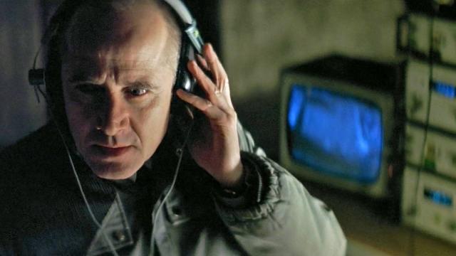still from "The Lives of Others" with an actor wearing 1980s headphones with a crt tv and monitoring equipment in the background
