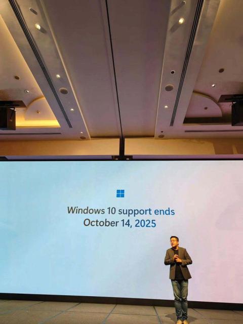 A Microsoft employee is seen standing in front of a big screen that says, "Windows 10 support ends October 14, 2025".