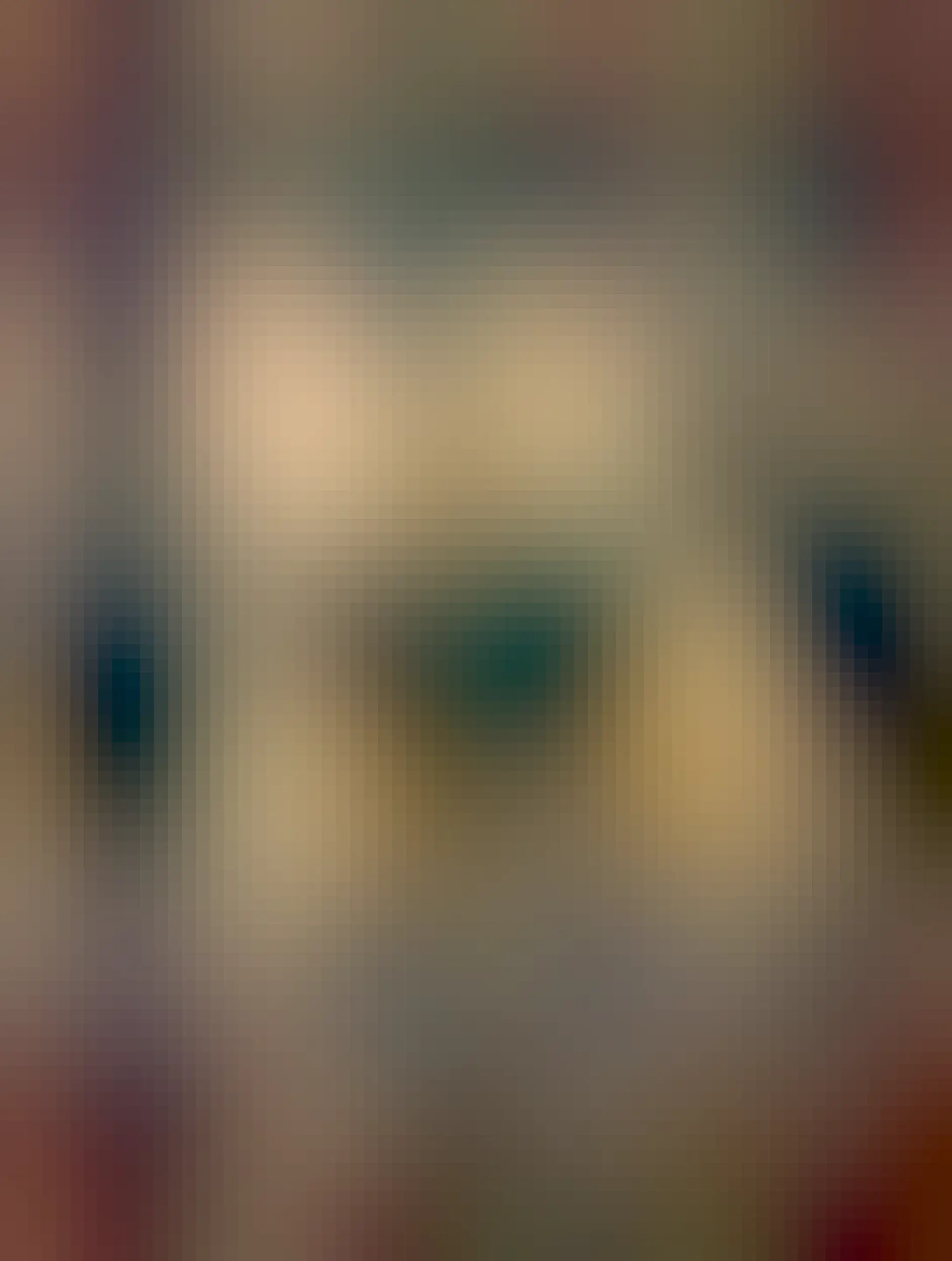 A close-up of an orange tabby cat lounging on a dark surface, with alert green eyes and a focused expression. The background features a soft, blurred gray curtain.