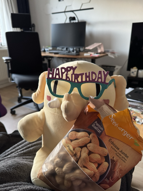 A Plushtodon with coloured „Happy Birthday“ glasses and a big bag of peanuts.