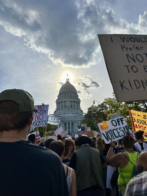 The Wisconsin state capitol, backlit by the sun with a huge crowd of creative and passionate protesters out in support of democracy.