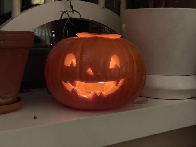 A small pumpkin with a smiling face lit up from the inside by a tea candle on a windowsill. 