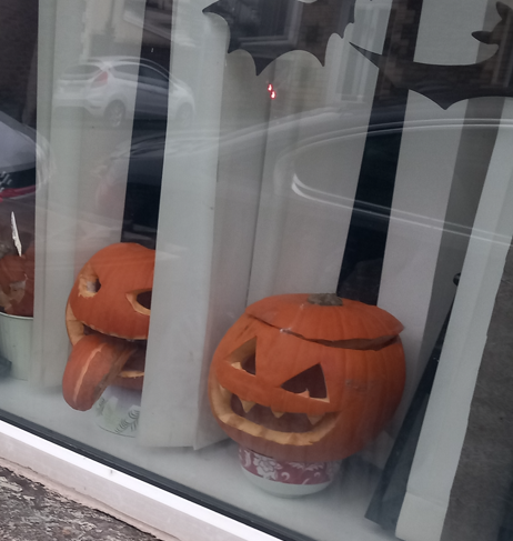 Two carved Halloween pumpkin heads on a windowsill, one with part of the rind sticking out of the mouth like a tongue.