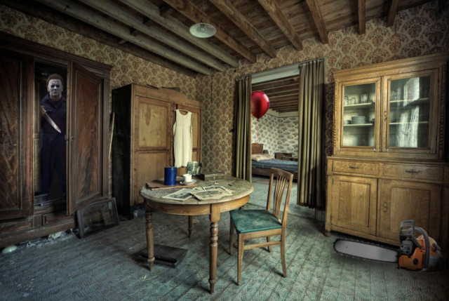 A dining room which is very shabby with faded brown floral wallpaper, an exposed timber ceiling and a worn green carpet. There is a table in the middle of the room with a worn green chair. There is a cupboard and someone has photoshopped in Jason with a white mask and a knife. There is a chainsaw photoshopped into the right corner of the image, and a red balloon in the doorway to the next room .