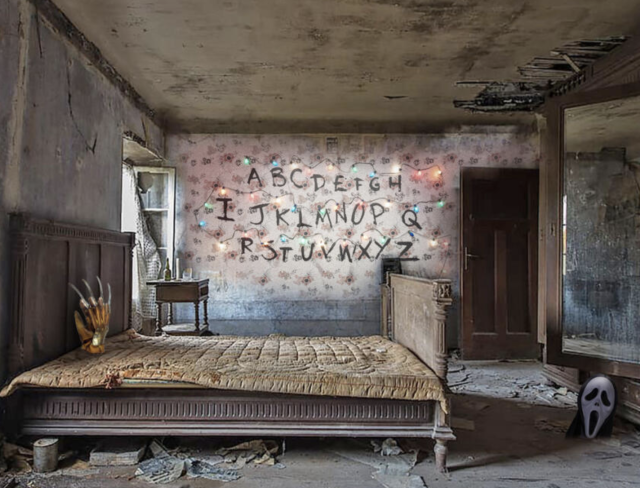 A shabby bedroom that has the walls and ceiling falling apart, and faded floral wallpaper and an old bed with various debris under it. On the bed is photoshopped a glove that looks like Freddy Kruger's, and on the wall is a sloppily looking alphabet as if by a child's hand. There is also the mask from the movie Scream in the lower corner. 